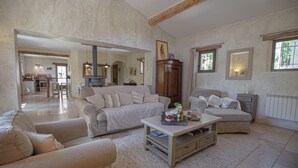 A spacious living room with a large sofa, a coffee table, and a dining area in the background. - Le mas des oliviers de Rustrel with swimming pool (Rustrel)