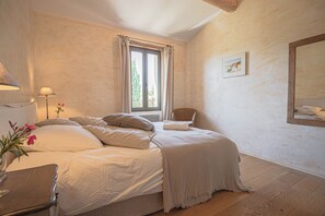Une chambre à coucher avec un lit, une chaise, une fenêtre avec des rideaux, une lampe et un tableau au mur.