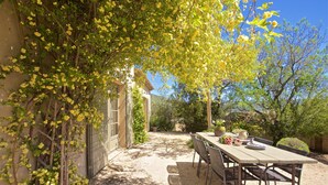 A patio with a table and chairs, surrounded by greenery and a building. - Le mas des oliviers de Rustrel with swimming pool (Rustrel)