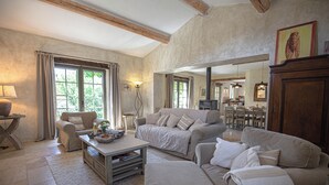 A spacious living room with a large sofa, a coffee table, and a fireplace. There is a dining area in the background with a table and chairs. - Le mas des oliviers de Rustrel with swimming pool (Rustrel)