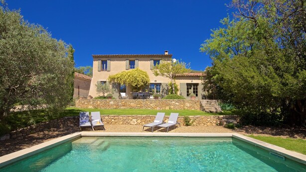 A swimming pool with two lounge chairs, a stone wall, and a building with a tiled roof in the background. - Le mas des oliviers de Rustrel with swimming pool (Rustrel)