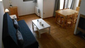 Een gezellige woonkamer met een bank, een eettafel en een televisie aan de muur.