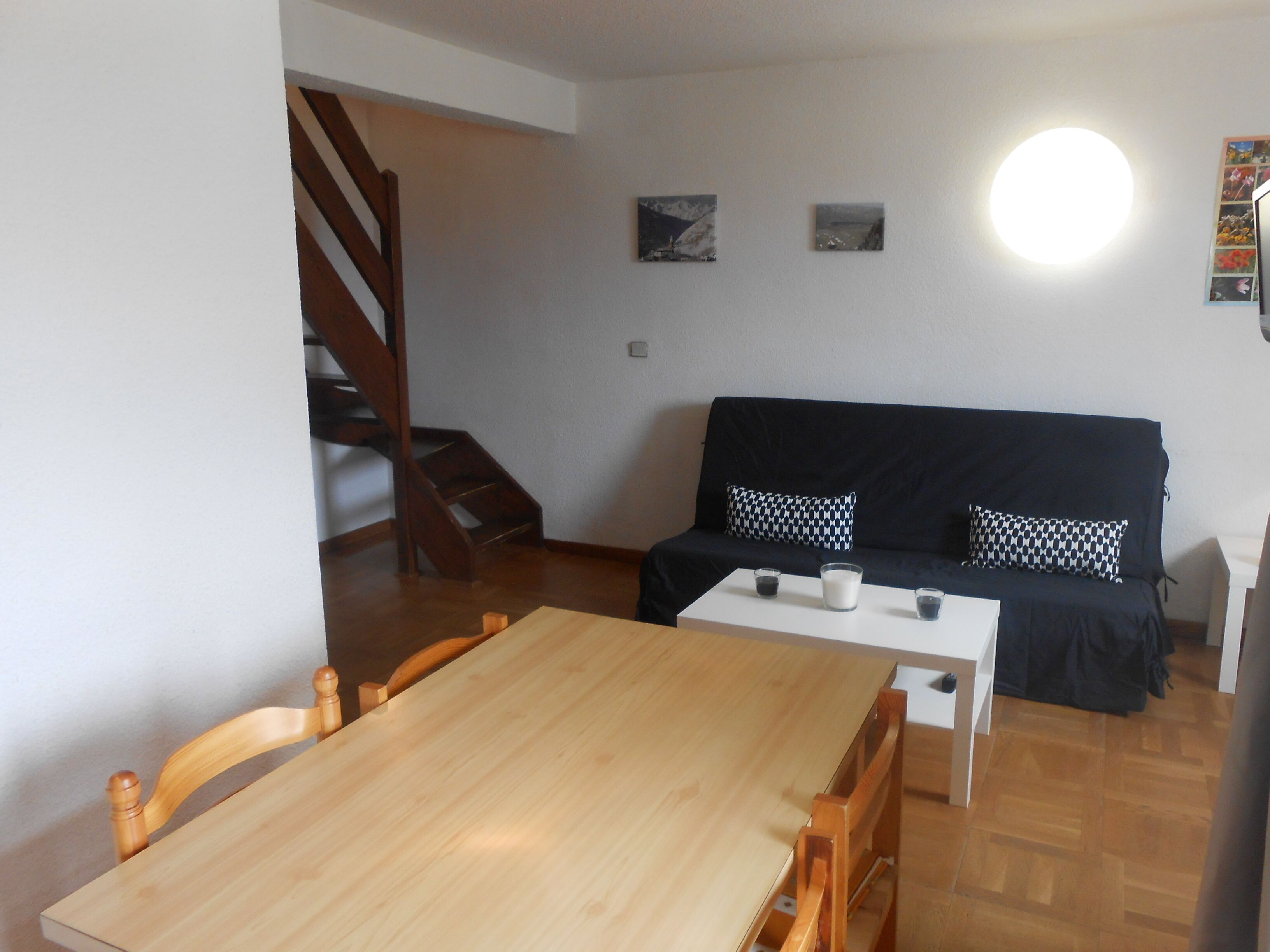 Een gezellige woonkamer met een houten eettafel, een zwarte bank met gestreepte kussens, en een trap naar een hoger niveau.