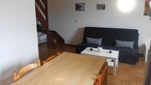 Een gezellige woonkamer met een houten eettafel, een zwarte bank met gestreepte kussens, en een trap naar een hoger niveau.