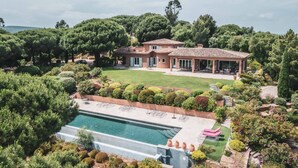 Una casa grande con piscina, rodeada de abundante vegetación y árboles.