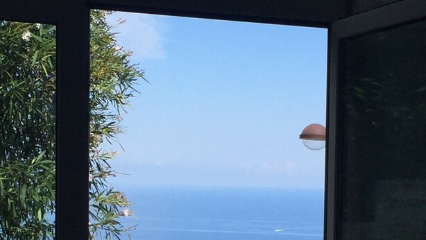 Un patio con pavimento in pietra, un tavolo e due sedie. Vasi con piante su un davanzale in pietra.