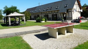 A building with a sloped roof, a covered seating area, and a ping pong table in the foreground.