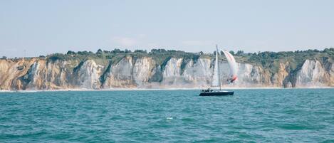 Un velero en un mar tranquilo con una costa rocosa al fondo.