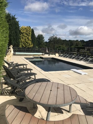 A pool area with lounge chairs, a wooden table, and a statue.
