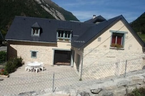 A stone building with a sloped roof, a fenced patio with outdoor seating, and a mountainous backdrop. - CAUTERETS Chalet La Grange (sleeps 2–11) in a quiet neighborhood, with parking (Cauterets)