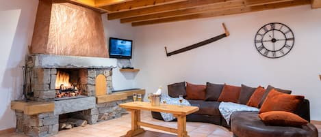 Una sala de estar acogedora con chimenea de piedra, techo de madera, televisor montado en la pared y un gran reloj.