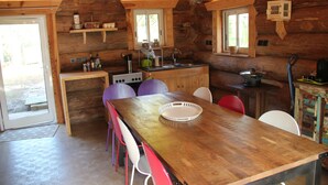 Ein Holzblockhaus-Interieur mit einem Esstisch, Stühlen, einer Küchenzeile mit Spüle und einem Fenster.