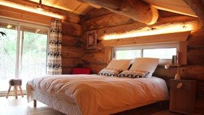 Ein Schlafzimmer einer Holzhütte mit Bett, Fenster und Nachttisch.