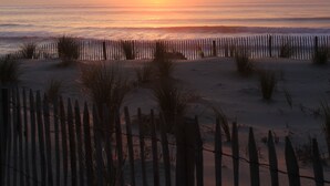 Ein Sonnenuntergang über einem Strand mit einer Holzfence und Sanddünen.