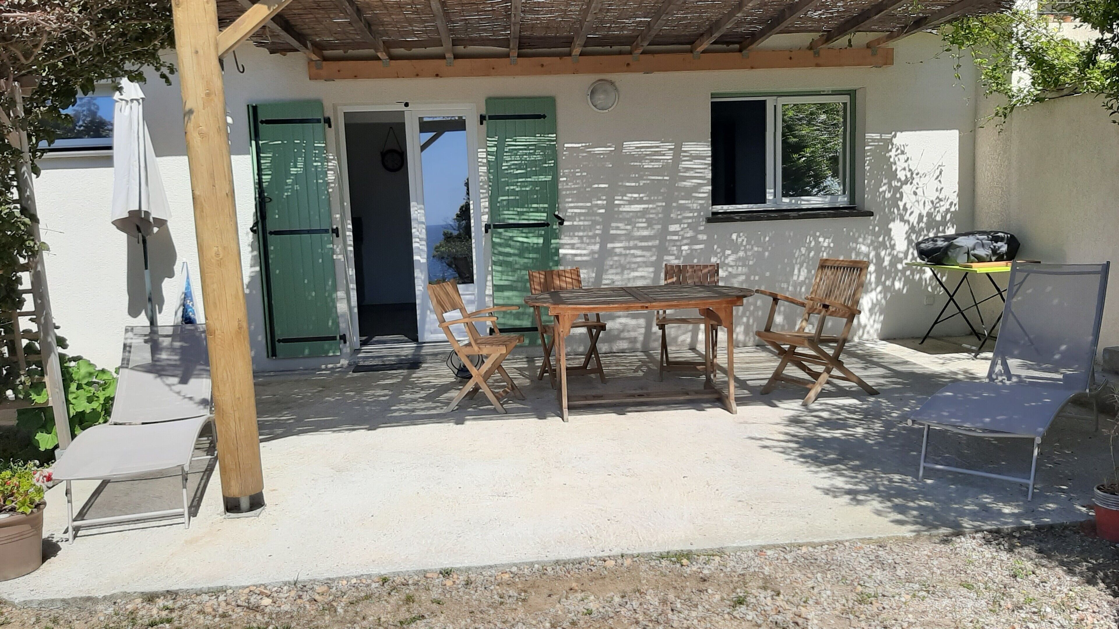 A covered patio with a wooden table and chairs, a small table with a chair, and a window with a view.