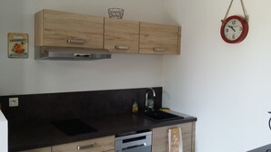 A kitchen with wooden cabinets, a black countertop, a sink, and a red wall clock. - RENT STUDIO 30 m² fully equipped  (Coggia)