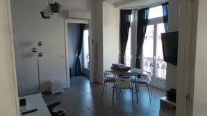 Ein modernes Wohnzimmer mit Essbereich, Fernseher und einem Balkon mit Vorhängen.
