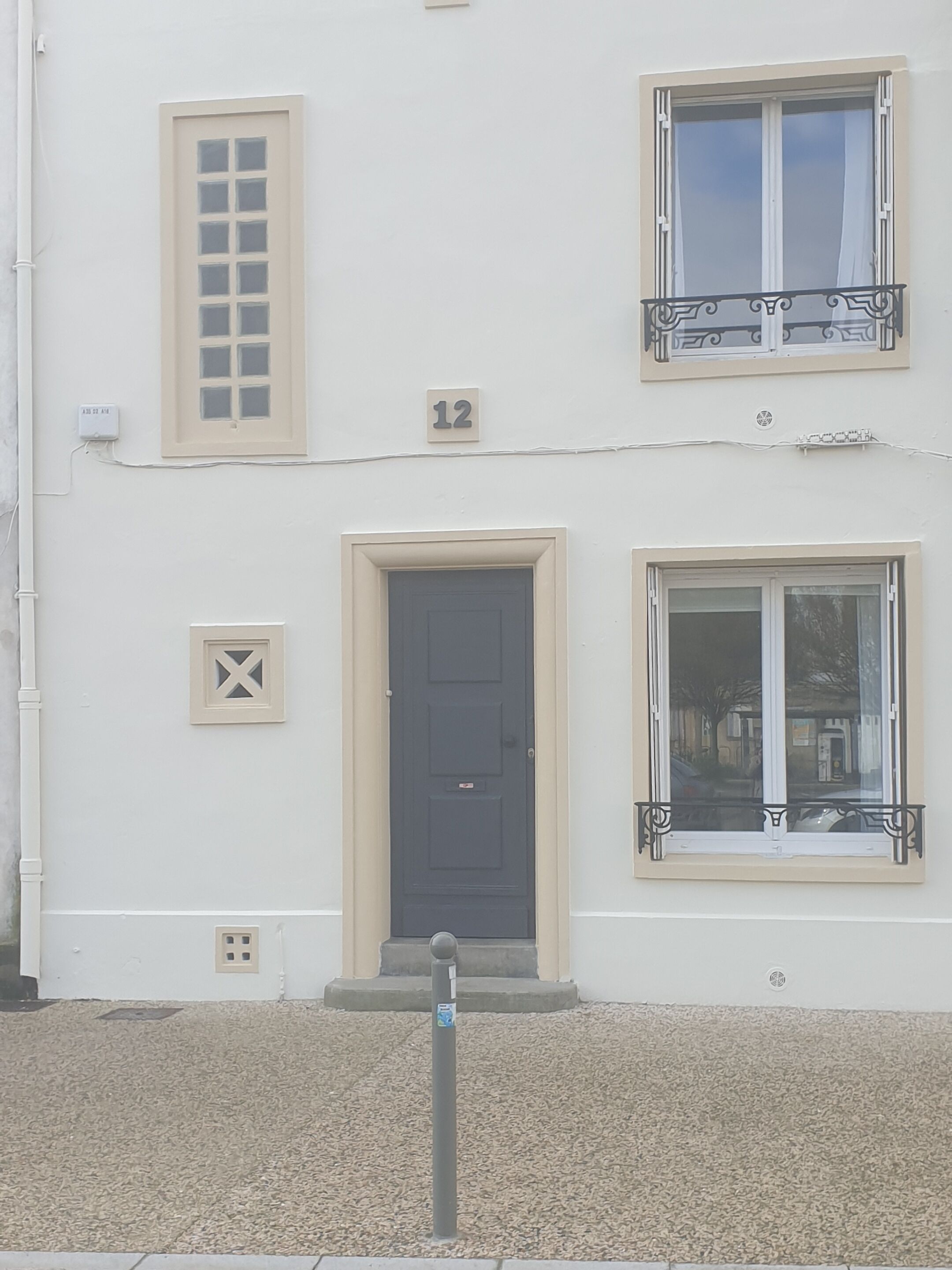 A building with a beige facade, a dark-colored door, and two windows with decorative frames.