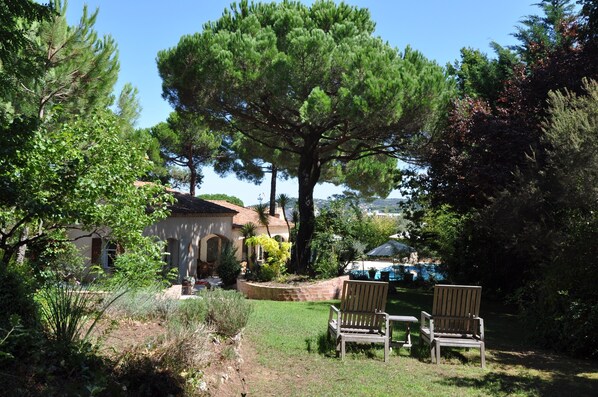 Una casa con un grande albero nel giardino, due sedie di legno e un patio.