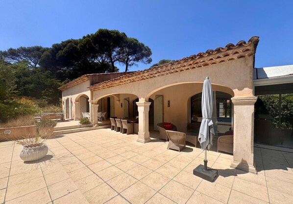 A covered outdoor patio with tiled flooring, white wicker furniture, and a pergola with a white umbrella. - GASSIN, 6 km from Saint-Tropez, exceptional villa for 8 people (Gassin)