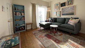 A living room with a grey sofa, a small round table, a bookshelf, and a patterned rug. - Studio 2 blocks to Beach w/ Parking - Close to LAX (Manhattan Beach)