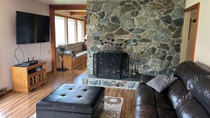 A living room with a stone fireplace, a leather sofa, a wooden entertainment unit, and a flat-screen TV.
