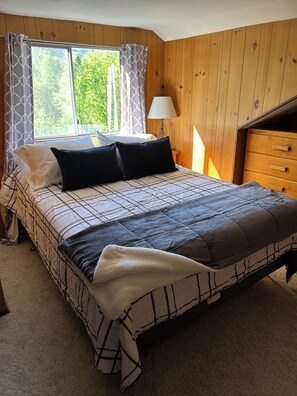 A bedroom with a bed, a nightstand, a lamp, and a window with curtains.