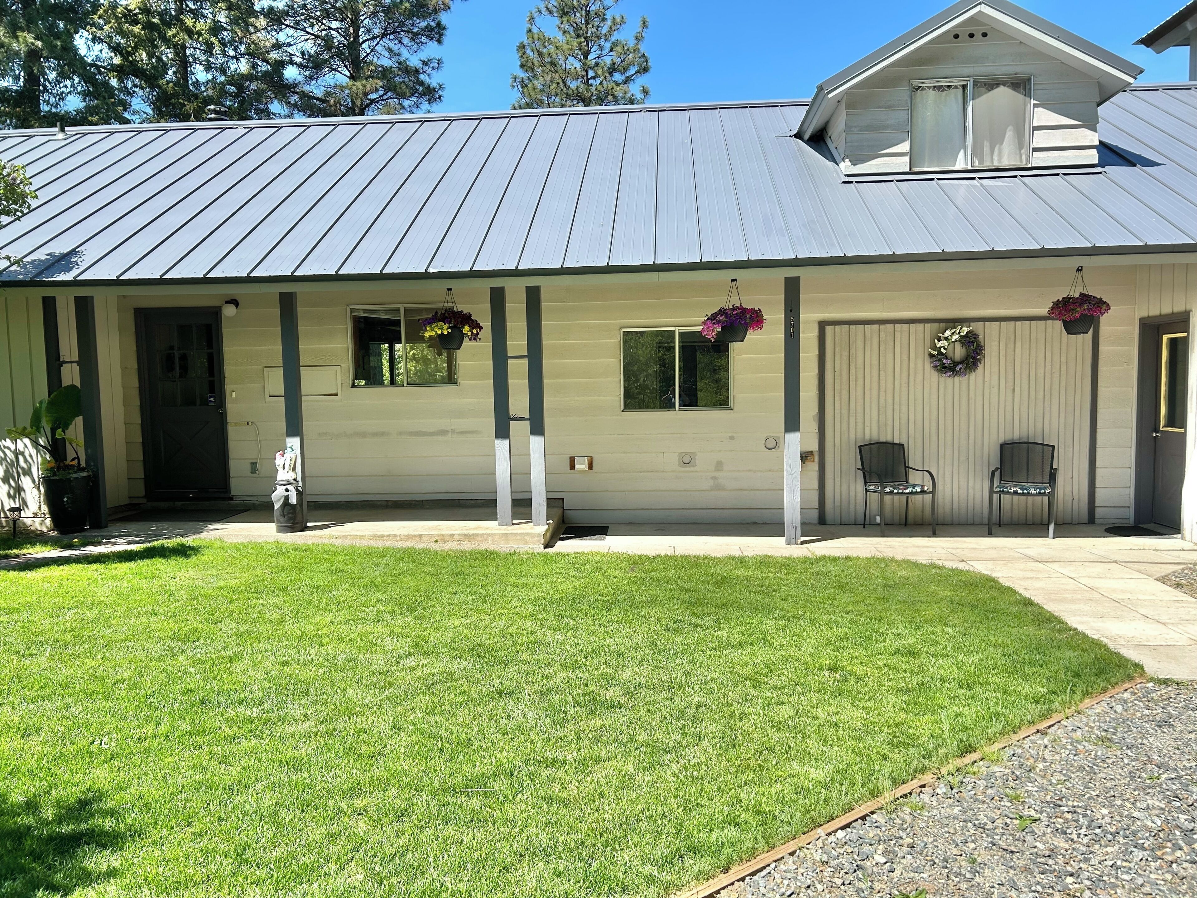 A single-story building with a metal roof, a front porch with two chairs, and a small front yard.