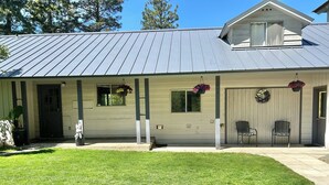 A single-story building with a metal roof, a front porch with two chairs, and a small front yard.