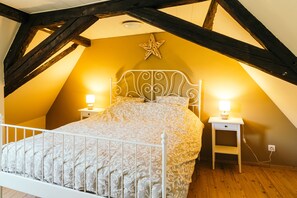 Ein Schlafzimmer mit schrägen Wänden, einem Bett mit gemustertem Überwurf, zwei Nachttischen mit Lampen und einer Stern-Dekoration an der Wand.
