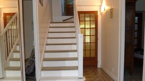 A staircase with white steps and a patterned carpet leading to a room with a wooden door and a light fixture on the wall.