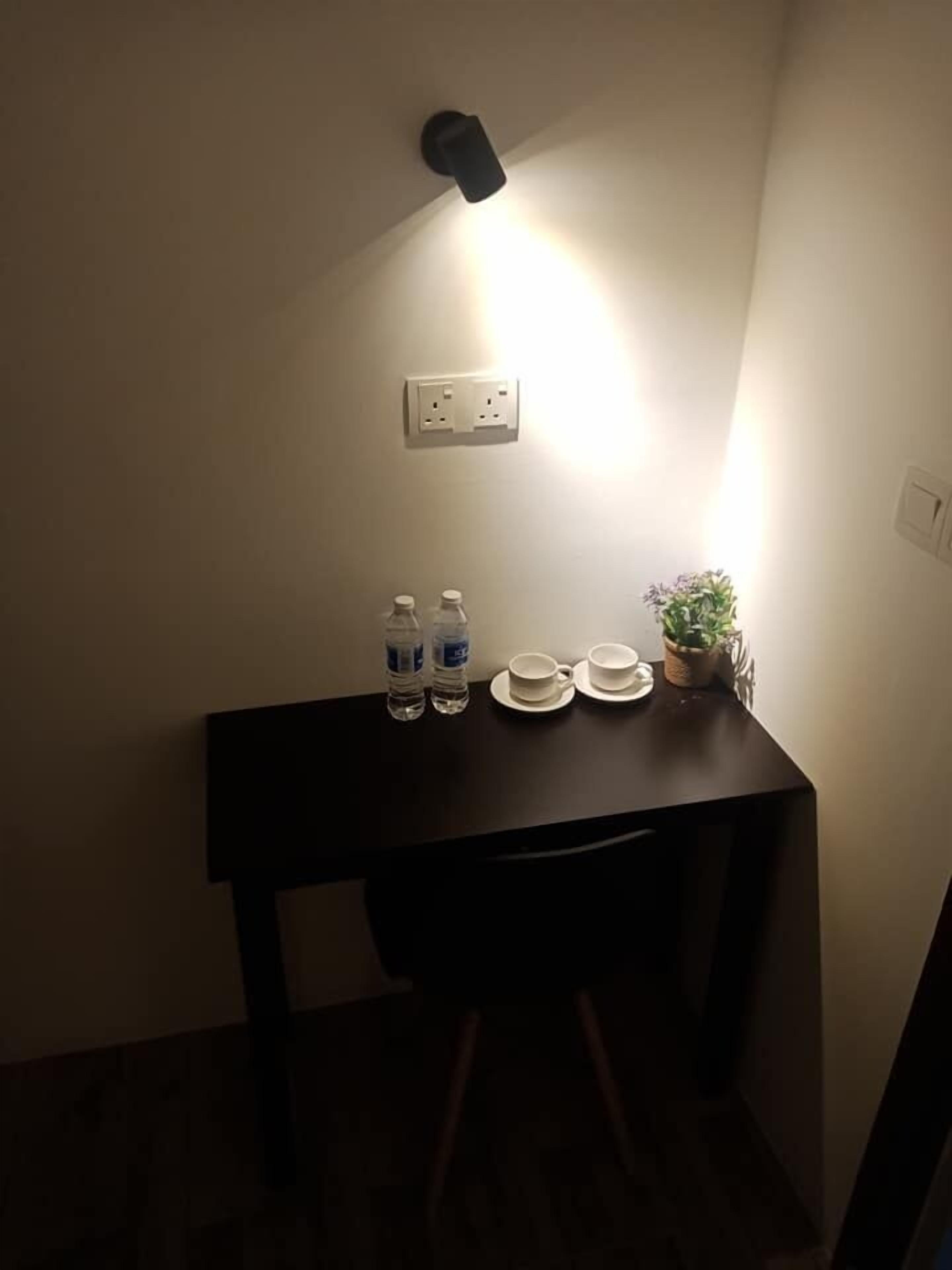 Une petite table en bois foncé, sur laquelle se trouvent deux bouteilles d’eau, deux tasses blanches et une plante en pot.