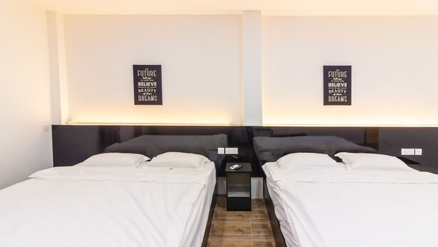A hotel room with two single beds, a small bedside table with a phone, and a wall-mounted light. - Tambun Warm Hotel (Ipoh)