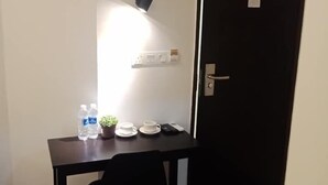 A small room with a dark wooden table, a black chair, a potted plant, a cup, a saucer, and two water bottles. - Tambun Warm Hotel (Ipoh)