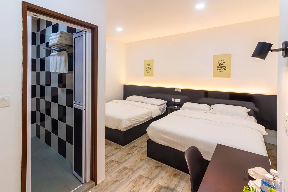 A hotel room with two beds, a desk, and a bathroom with a checkered mirror.