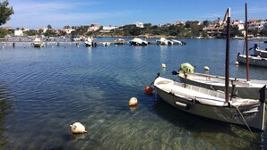 Ein Yachthafen mit mehreren vertäuten Booten, klarem Wasser und einer Kulisse aus Gebäuden und Hügeln.
