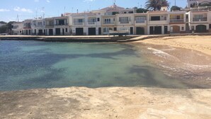Ein Küstengebäude mit mehreren Balkonen, einem Sandstrand und klarem Wasser.