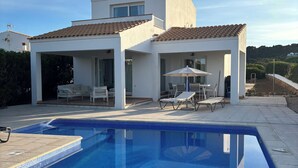 Ein modernes Haus mit Pool, Sitzgelegenheit im Freien und Blick auf die umliegende Landschaft.