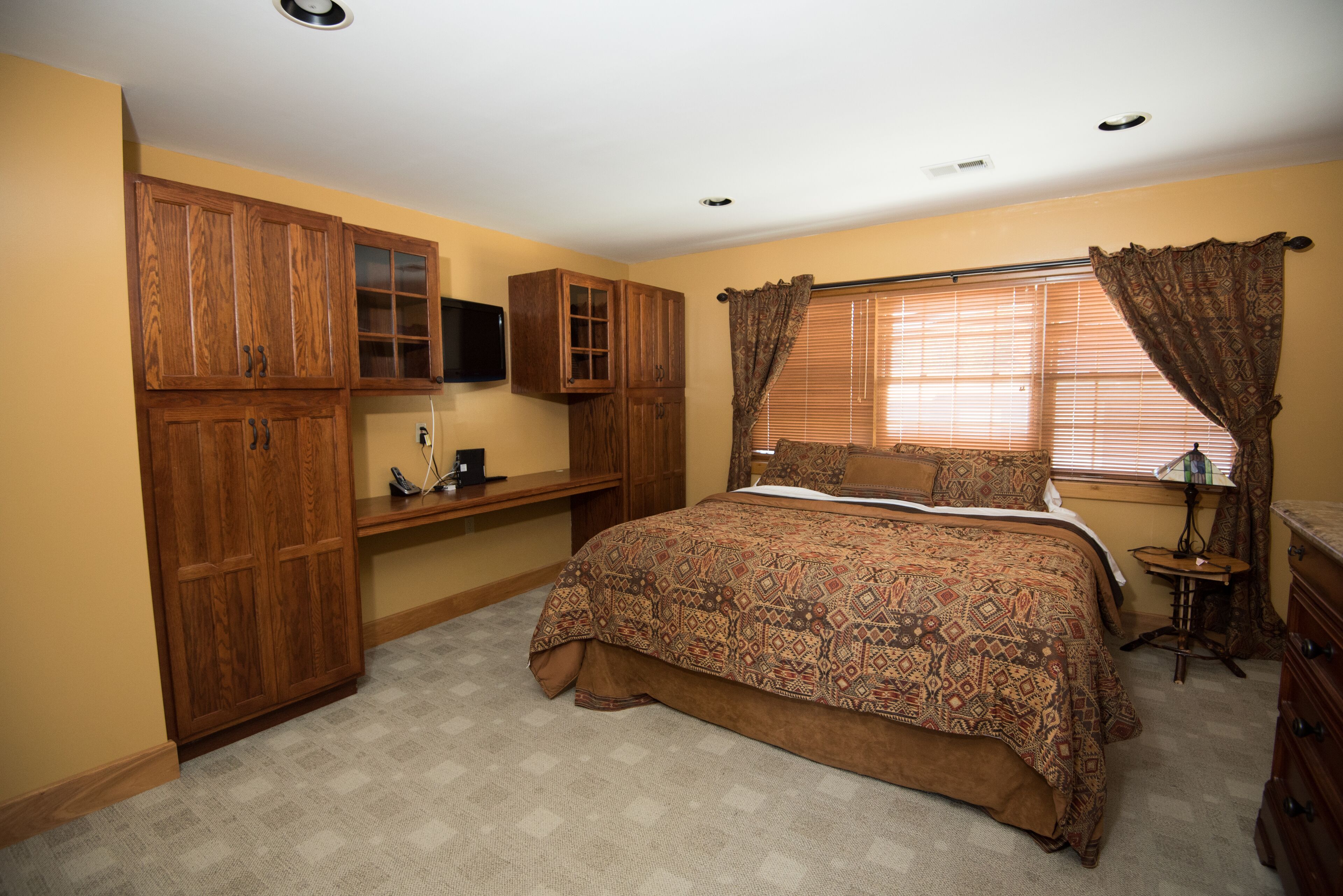 A bedroom with a large bed, wooden cabinets, a desk, and a window with curtains.