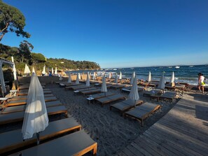 Un espace aménagé au bord de la plage, avec des chaises longues et des parasols, une terrasse en bois et une vue sur la mer.
