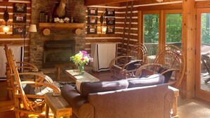 Interior rústico de una cabaña con chimenea de piedra, vigas de madera en el techo y una lámpara de asta de ciervo.