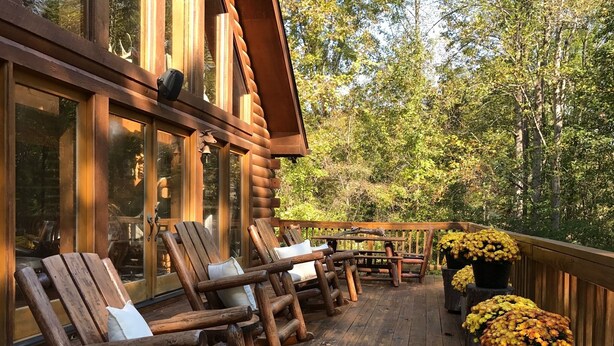 Una terraza de madera con sillas y mesas rústicas, rodeada de un bosque.