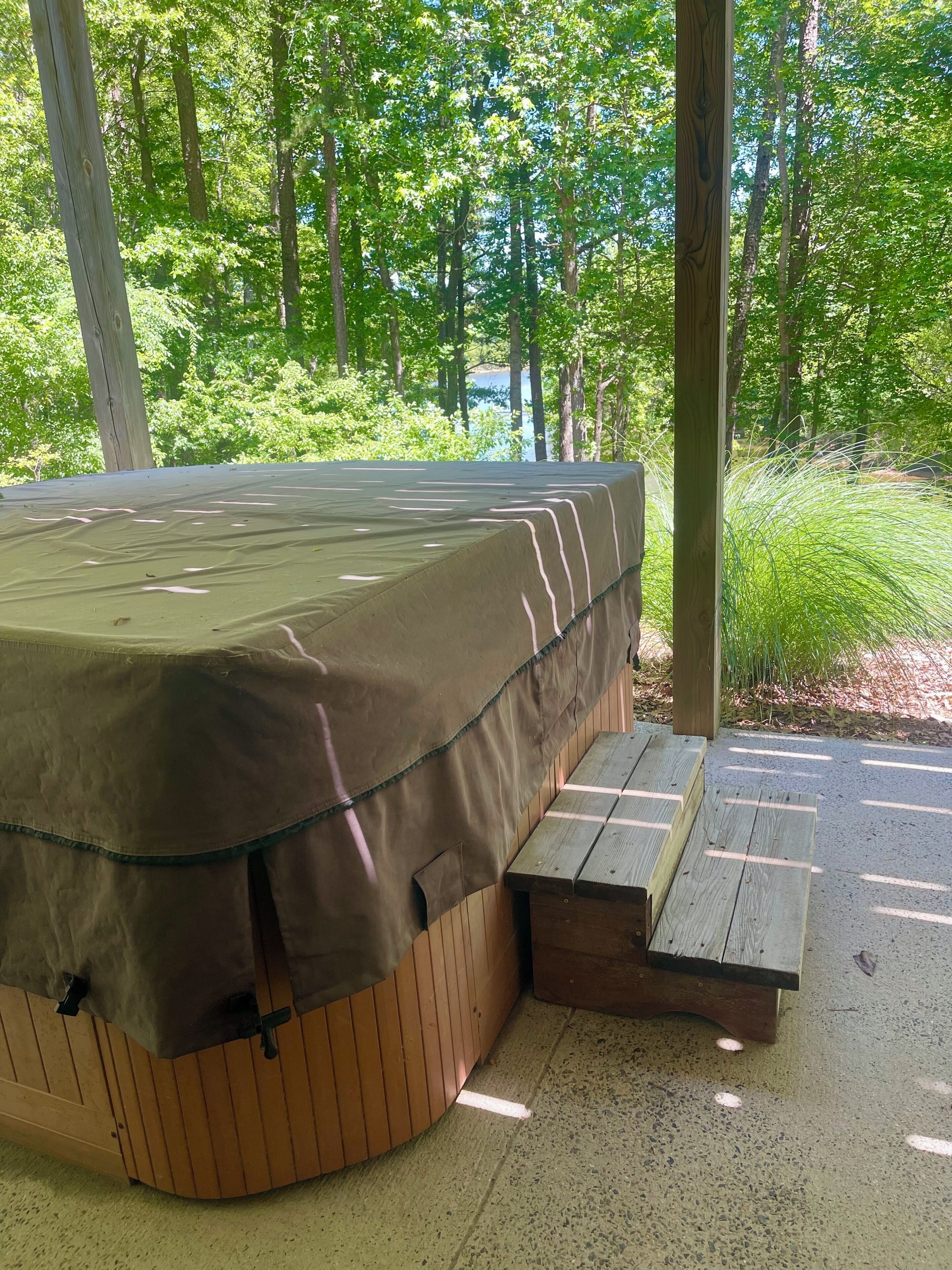 A covered outdoor sleeping area with a bench, surrounded by trees and a gravel path.