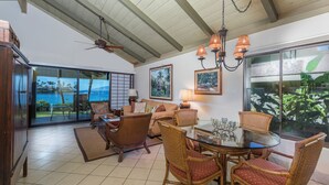 A spacious living area with a glass dining table surrounded by wicker chairs, a sofa, and a ceiling fan. - Napili Lani 320 2BD Luxury with Beach Access (Lahaina)