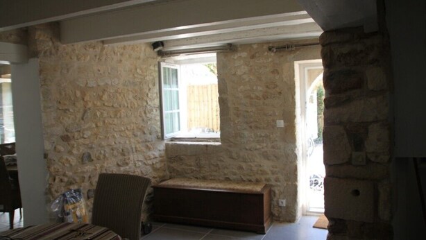 Une pièce aux murs de pierre, avec un banc, une chaise et une fenêtre.
