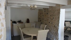 Un coin repas avec une table ronde et des chaises en osier, un mur en pierre et un lustre.