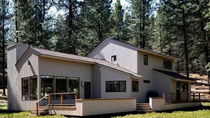 A modern two-story house with large windows, a deck, and a staircase leading to the entrance. - Air Conditioned/Unobstructed View of Golf Course (Black Butte Ranch)