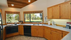 A kitchen with wooden cabinets, a stove, and a dishwasher. There are two windows with views of a green landscape. - Air Conditioned/Unobstructed View of Golf Course (Black Butte Ranch)