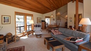 A spacious living room with a wooden ceiling, a grey sofa, a dining table, and a fireplace. - Air Conditioned/Unobstructed View of Golf Course (Black Butte Ranch)