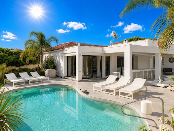 Un espace moderne aménagé au bord de la piscine, avec une piscine à eau claire, des chaises longues blanches et un coin salon abrité.